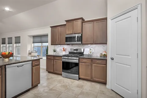 a kitchen with stainless steel appliances granite countertop a stove top oven a sink dishwasher and a refrigerator with wooden cabinets