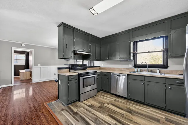 a kitchen with stainless steel appliances granite countertop a sink a stove top oven and wooden floors