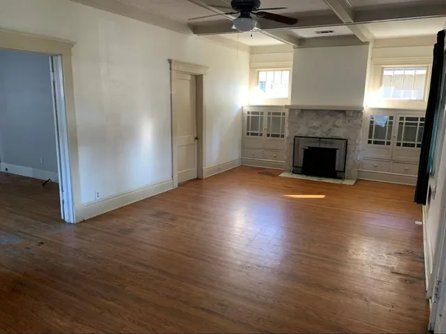 an empty room with wooden floor fireplace and windows