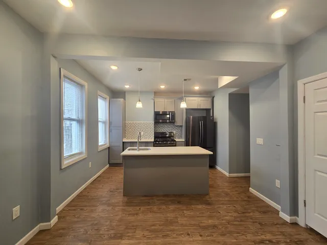 a living room with stainless steel appliances kitchen island granite countertop a refrigerator a sink a oven and white cabinets with wooden floor
