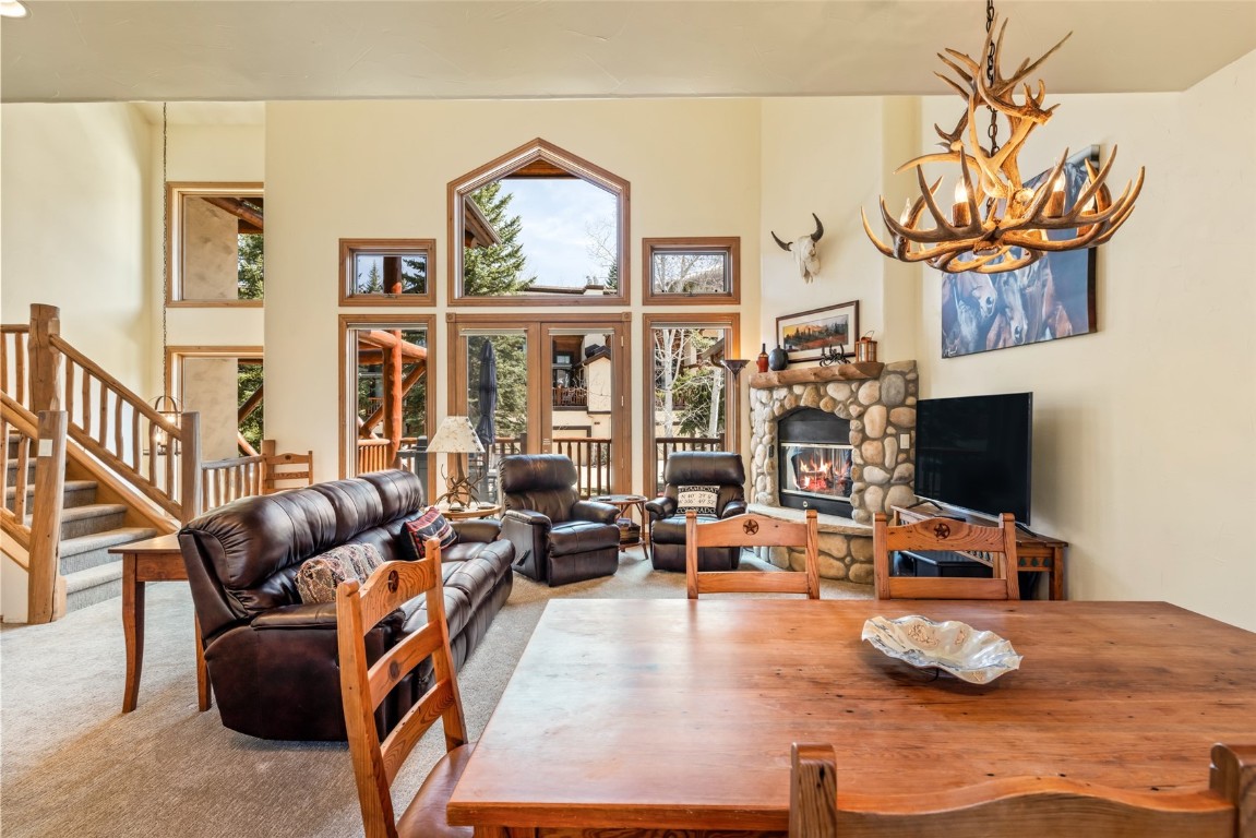 2685 Timber Court, Unit 2 Steamboat Springs, CO 80487 - Photo 7 of 31 Living room with a notable chandelier, a stone fireplace, carpet floors, stairway, and a towering ceiling