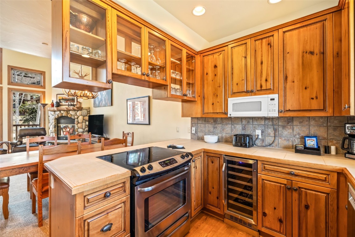 2685 Timber Court, Unit 2 Steamboat Springs, CO 80487 - Photo 9 of 31 Kitchen featuring white microwave, glass insert cabinets, a peninsula, stainless steel range with electric stovetop, and beverage cooler