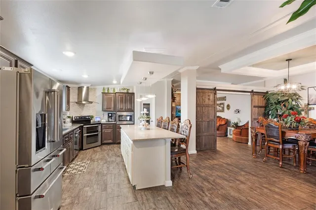 a kitchen with stainless steel appliances kitchen island granite countertop a table chairs sink and cabinets