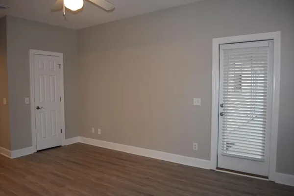 an empty room with wooden floor chandelier fan and windows