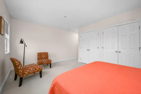 a bedroom with a bed a chair and potted plant on the dresser