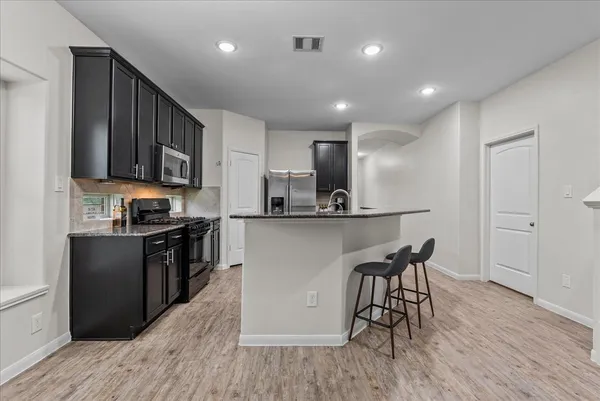 a kitchen with stainless steel appliances granite countertop wooden cabinets a refrigerator a stove a sink and a oven with wooden floor