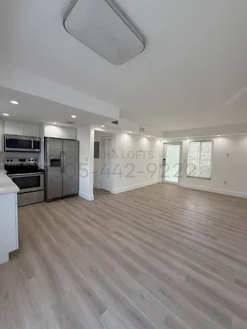 a view of an empty room with kitchen and window