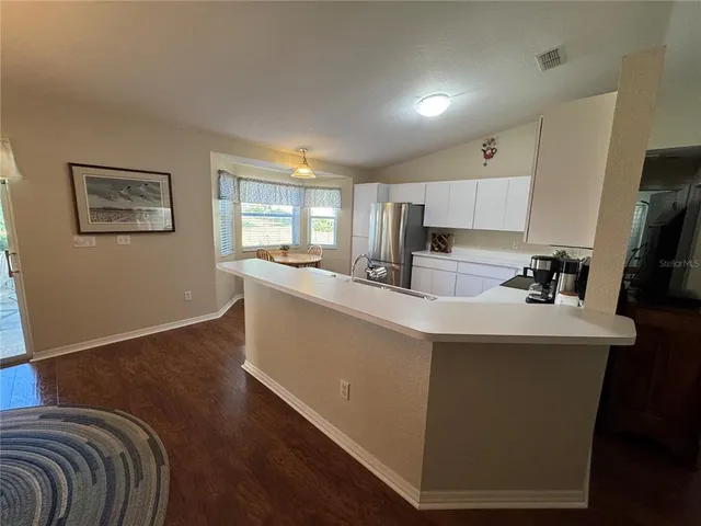 a living room with stainless steel appliances kitchen island granite countertop a sink a refrigerator and a stove with wooden floor