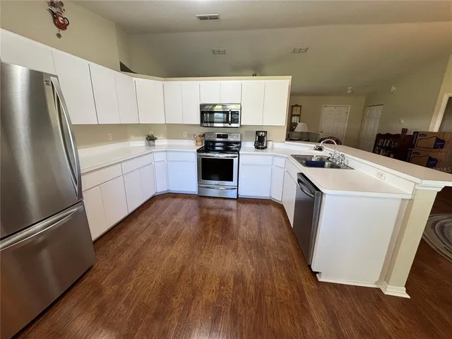 a kitchen with a refrigerator a stove top oven a sink and cabinets with wooden floor