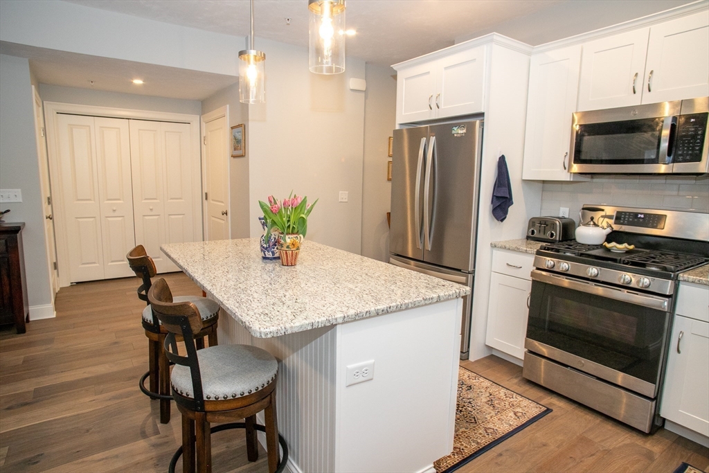 a kitchen with stainless steel appliances granite countertop a stove a refrigerator a microwave a sink a dining table and chairs with wooden floor