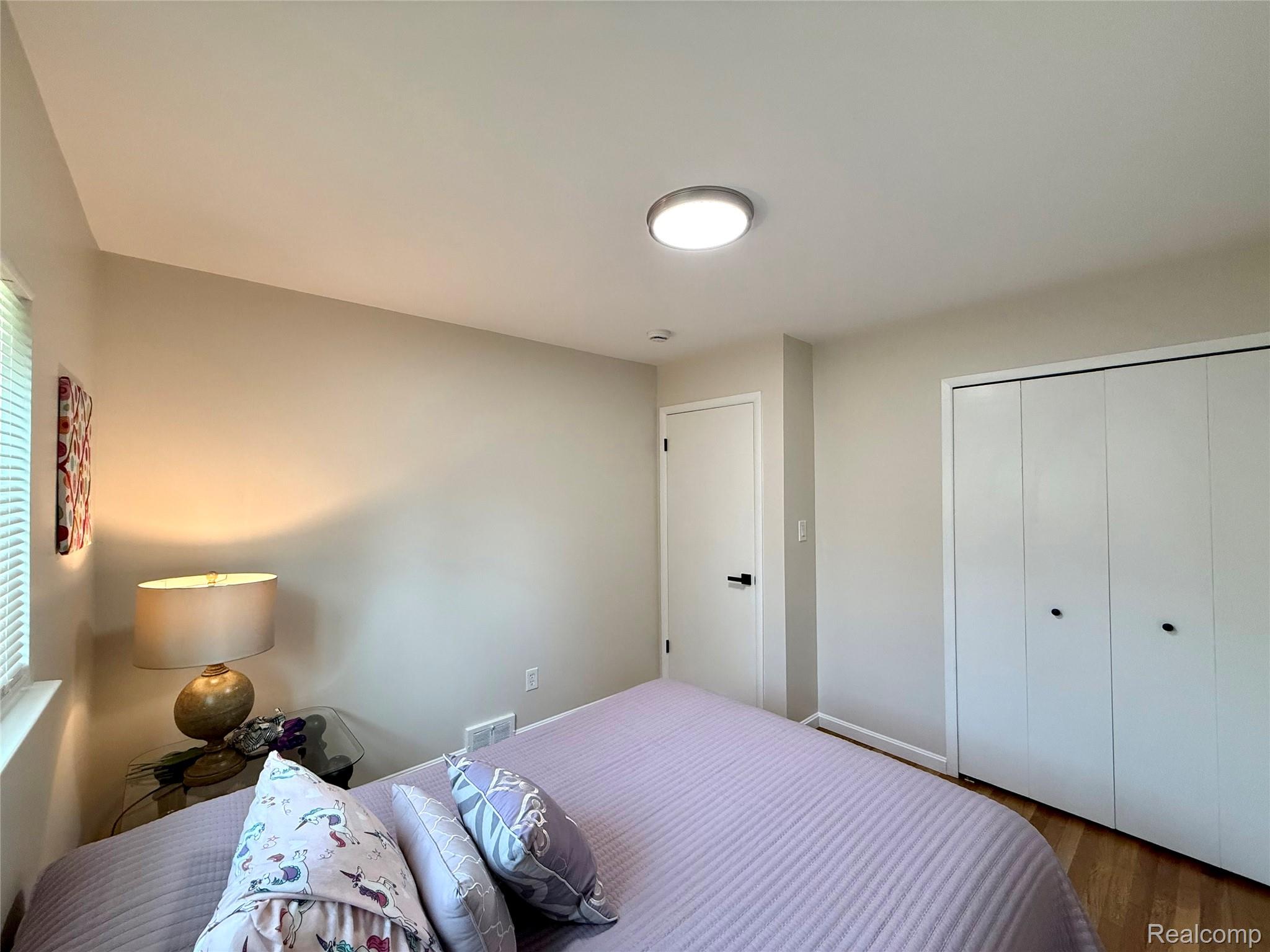 39909 Lynn Street Canton, MI 48187 - Photo 23 of 45 Bedroom featuring light neutral wall paint, wood-finish flooring, a flush-mount ceiling light fixture, a white interior door with a black handle, and white bi-fold closet doors with black pulls