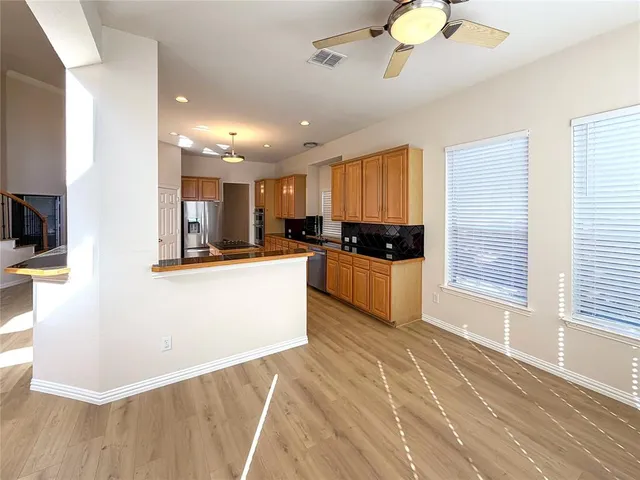 a kitchen with stainless steel appliances kitchen island granite countertop a refrigerator a stove a microwave oven with white cabinets and wooden floor