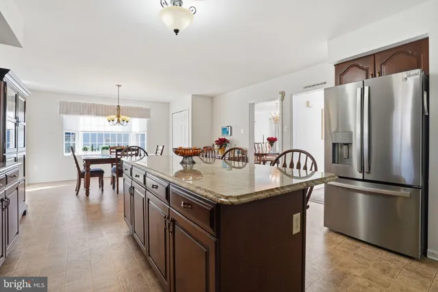 a kitchen with stainless steel appliances granite countertop a table chairs a refrigerator a sink a stove and a center island