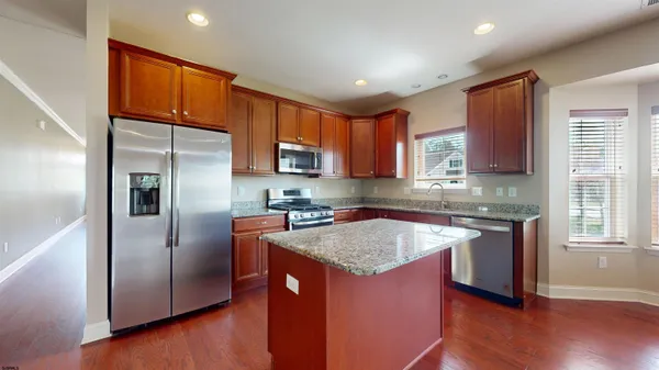 a kitchen with stainless steel appliances granite countertop a refrigerator a sink dishwasher a stove and white cabinets with wooden floor