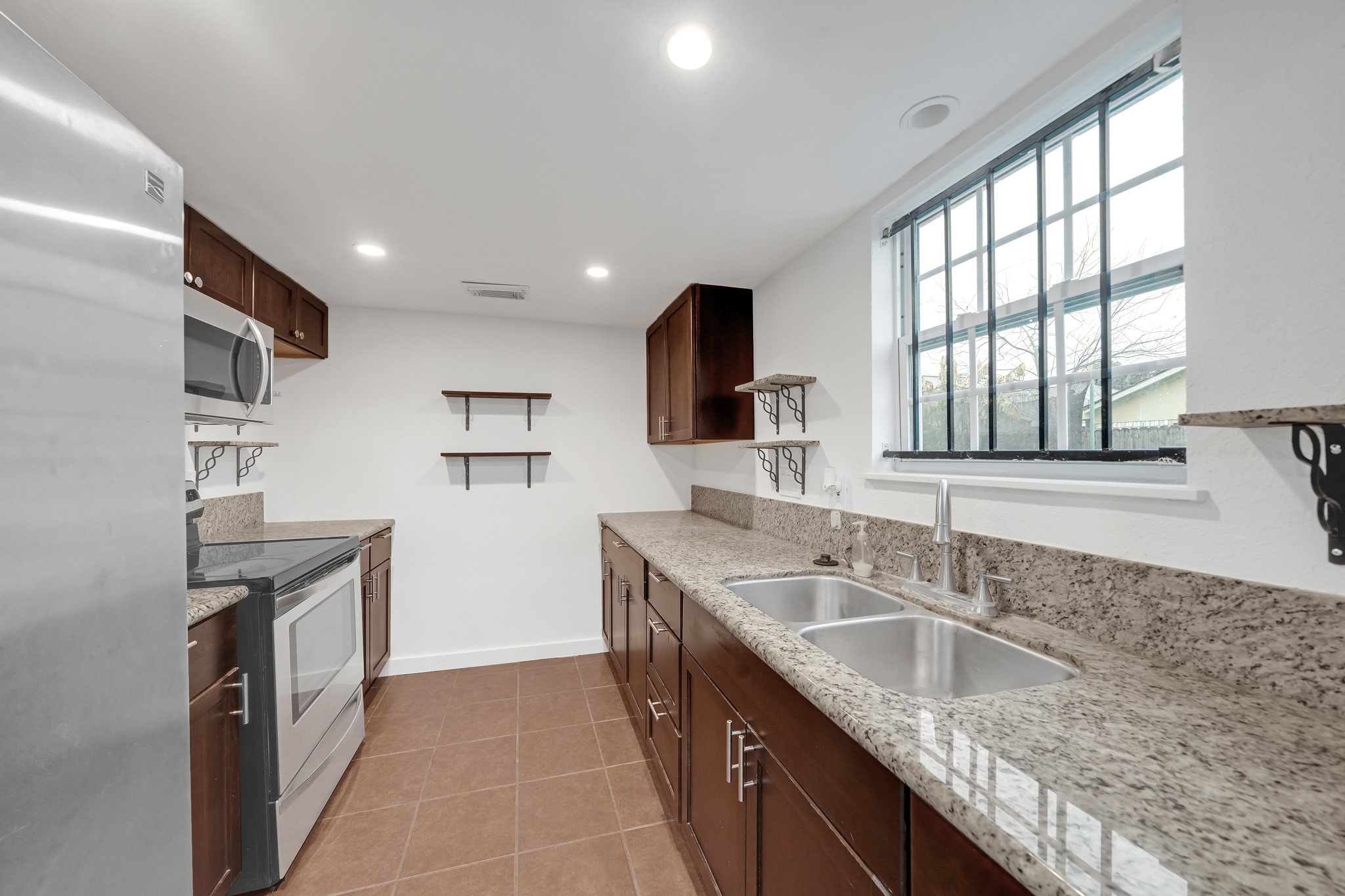 635 Walston Lane Houston, TX 77060 - Photo 11 of 24 Modern kitchen with granite countertops, stainless steel appliances, and ample cabinetry. Features include a double sink, tile flooring, and open shelving, with a large window providing natural light.
