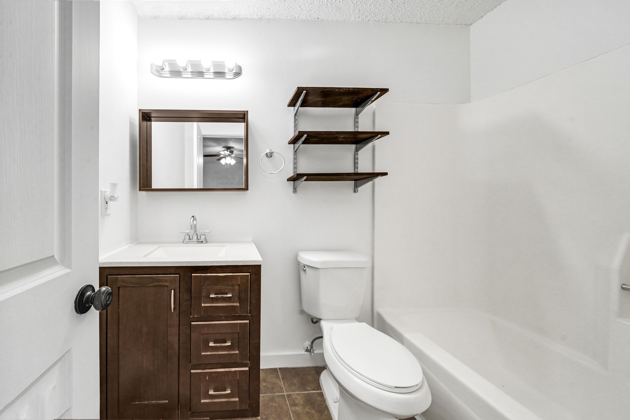 635 Walston Lane Houston, TX 77060 - Photo 18 of 24 This bathroom features a modern design with a dark wood vanity, a white countertop, and a matching mirror. It includes a toilet, a bathtub with a shower, and wall-mounted shelves for extra storage. The space is well-lit and has a clean, contemporary feel.