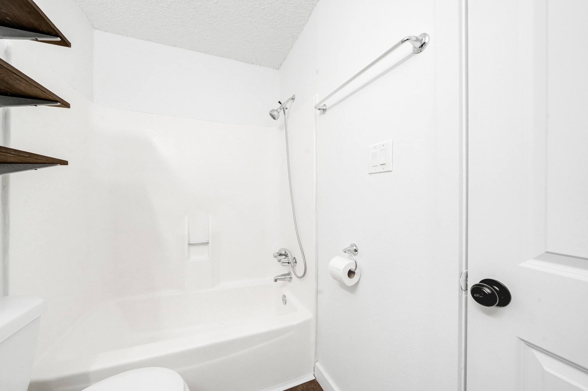 635 Walston Lane Houston, TX 77060 - Photo 20 of 24 This is a clean, white bathroom featuring a bathtub with a showerhead, a towel rack, toilet paper holder, and dark wood shelves. The design is simple and functional.