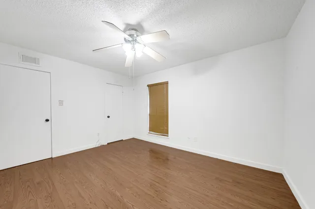 a view of an empty room with wooden floor and a ceiling fan