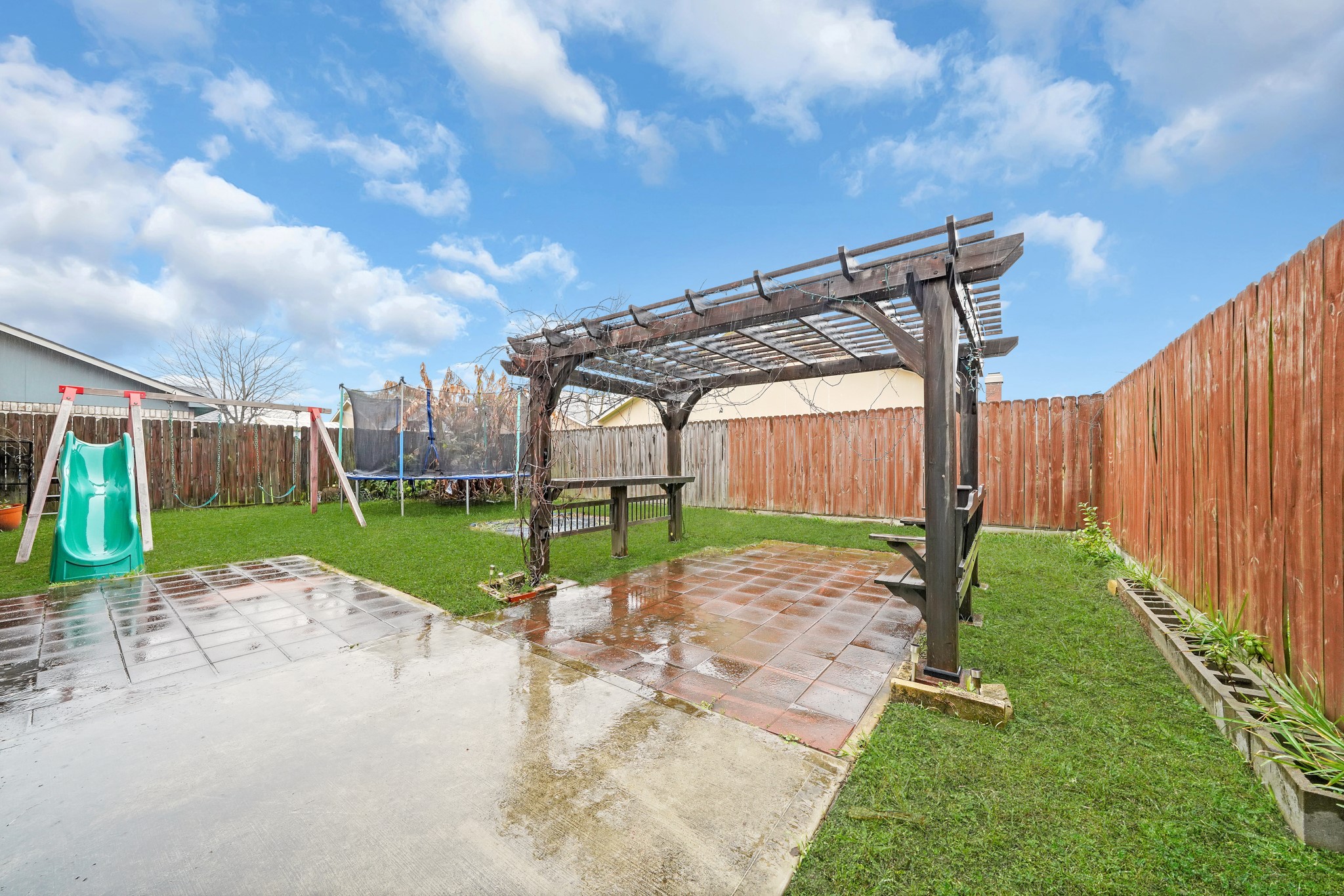635 Walston Lane Houston, TX 77060 - Photo 23 of 24 Spacious backyard with a wooden pergola over a tiled patio, perfect for outdoor gatherings. Features a play area with a slide and a trampoline, surrounded by a wooden fence for privacy.