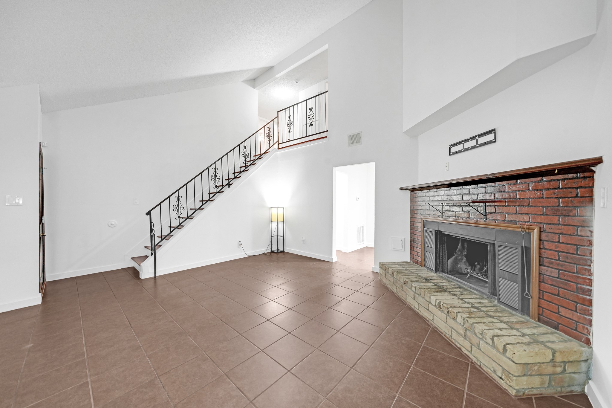 635 Walston Lane Houston, TX 77060 - Photo 4 of 24 This spacious living area features high ceilings and a classic brick fireplace. The room has a tiled floor and an elegant staircase with decorative railing. It's bright and inviting, offering a great space for relaxation or entertaining.