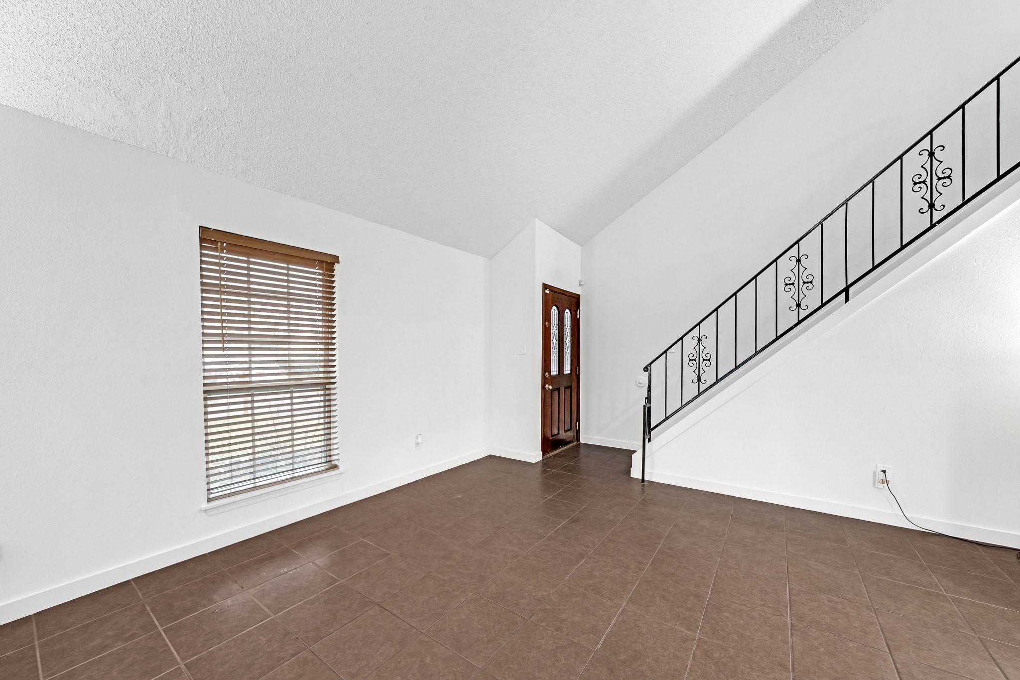 635 Walston Lane Houston, TX 77060 - Photo 5 of 24 Bright living space with high ceilings, tiled floors, and a large window with wooden blinds. Features a decorative iron staircase leading to the upper level.
