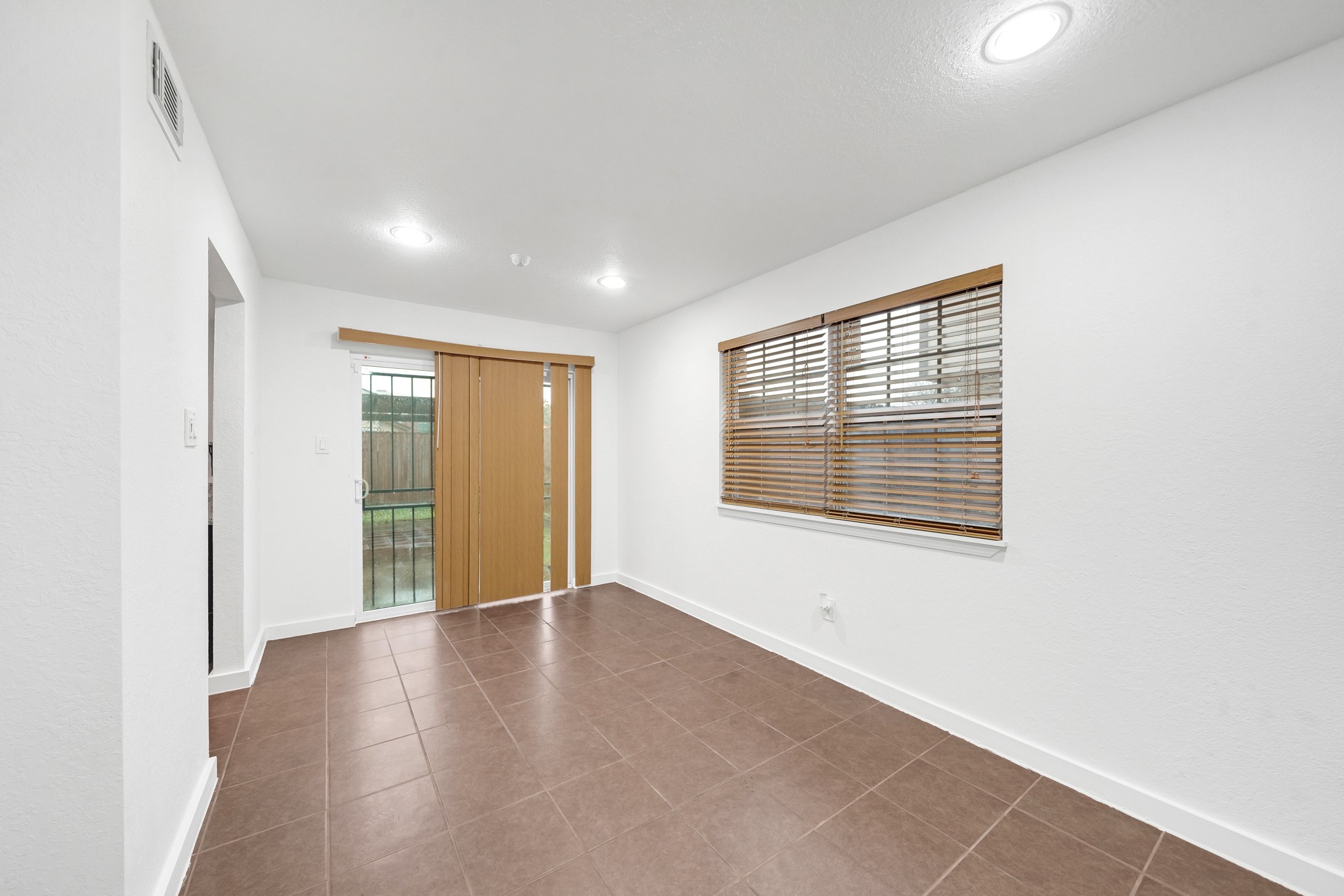 635 Walston Lane Houston, TX 77060 - Photo 7 of 24 This room features clean white walls and a brown tiled floor, with ample natural light from a large window and sliding glass door leading to a fenced backyard. Ideal for a cozy living or dining space.