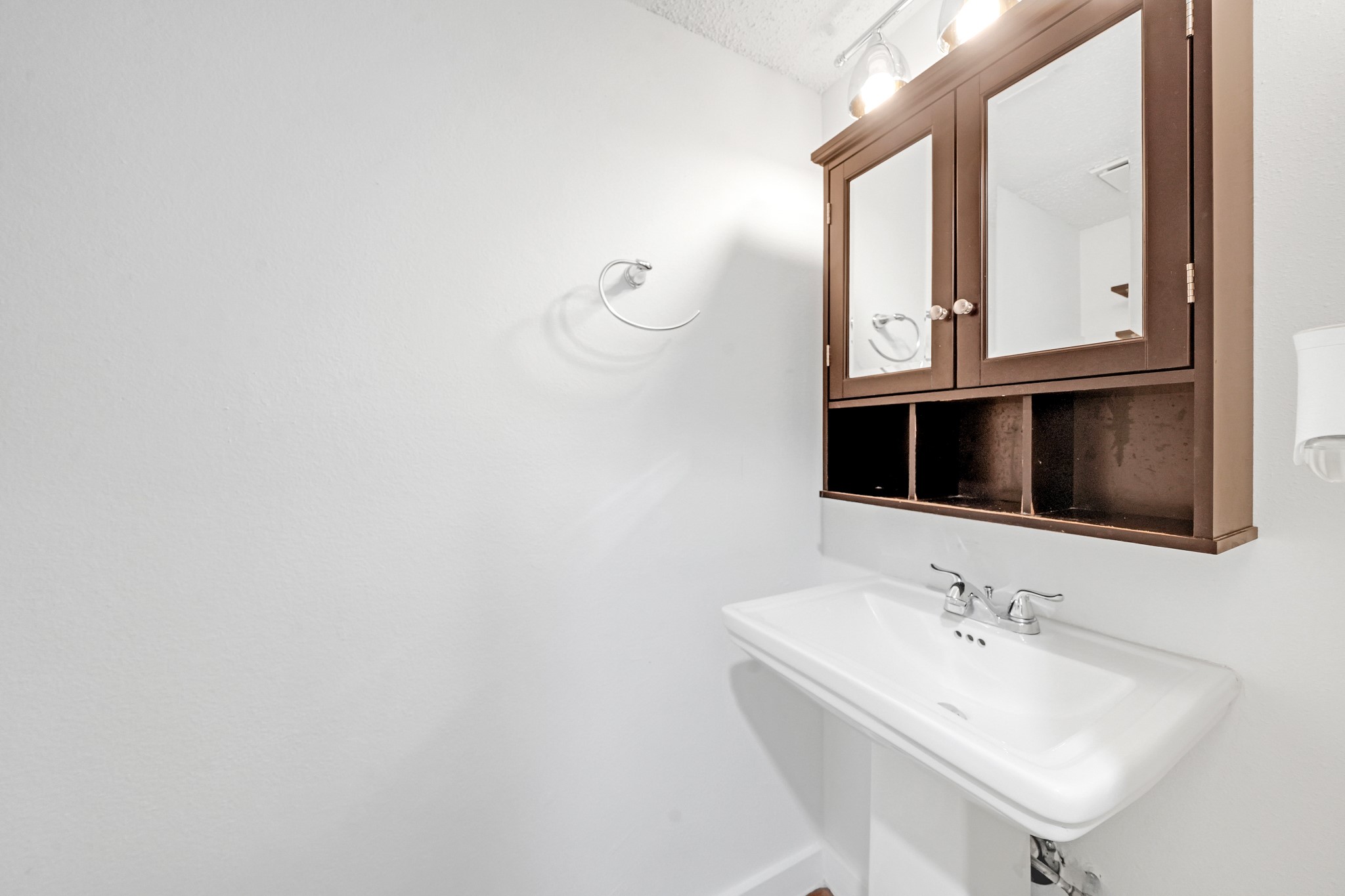 635 Walston Lane Houston, TX 77060 - Photo 8 of 24 This bathroom features a clean, minimal design with a modern white sink and a dark wood cabinet with mirrored doors for storage. Bright lighting enhances the space.