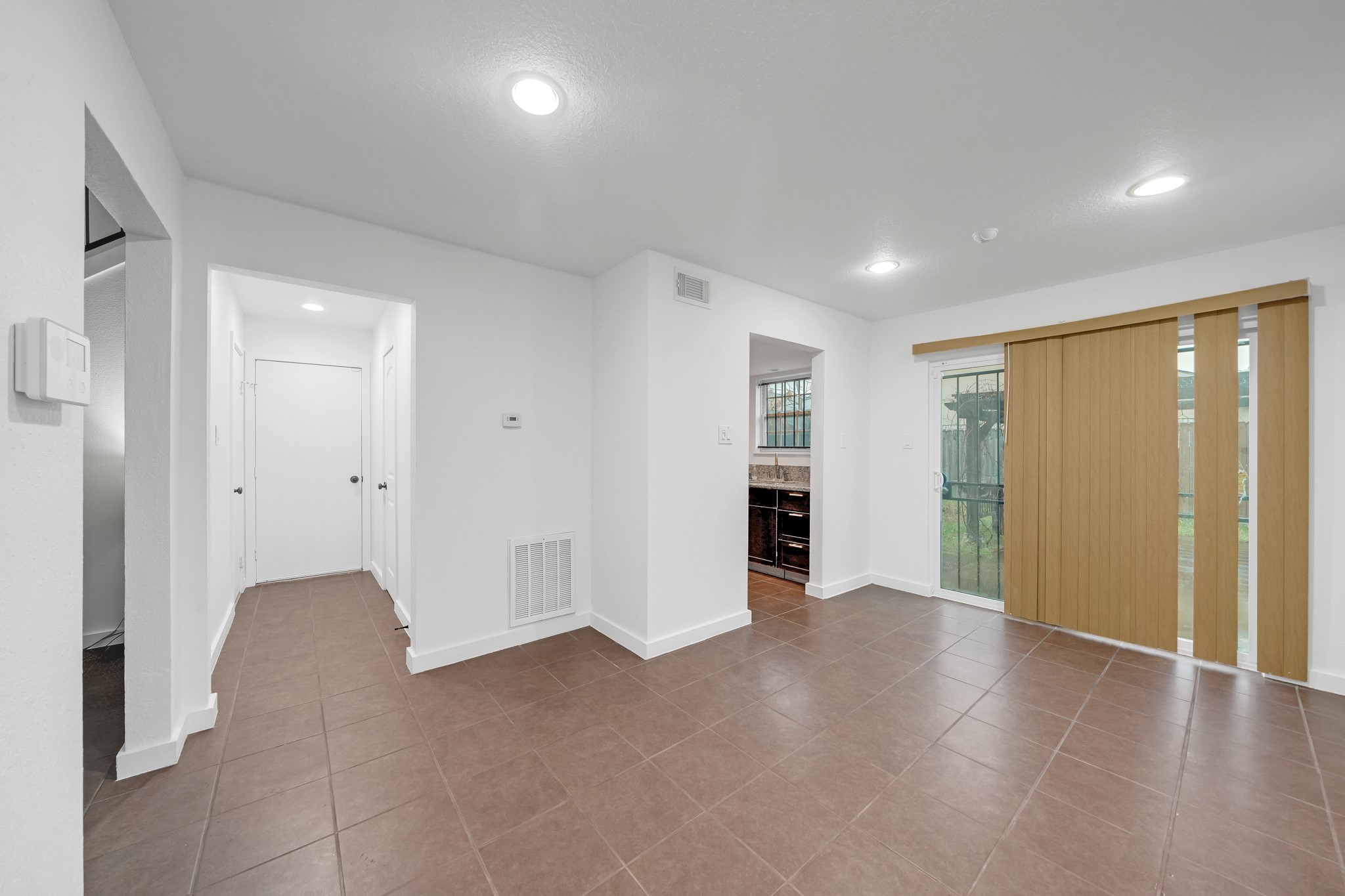 635 Walston Lane Houston, TX 77060 - Photo 9 of 24 This photo shows a bright, open living space with tiled flooring, recessed lighting, and sliding glass doors with vertical blinds. There's a view into the adjacent kitchen, and a hallway leading to other rooms. The space feels modern and functional.