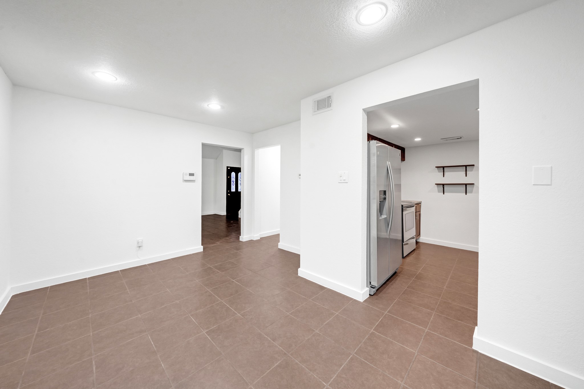 635 Walston Lane Houston, TX 77060 - Photo 10 of 24 This photo showcases a bright open-plan space with tiled flooring and recessed lighting. It leads to a kitchen area featuring modern appliances and minimalist shelving. The white walls and clean lines offer a blank canvas for personalization.