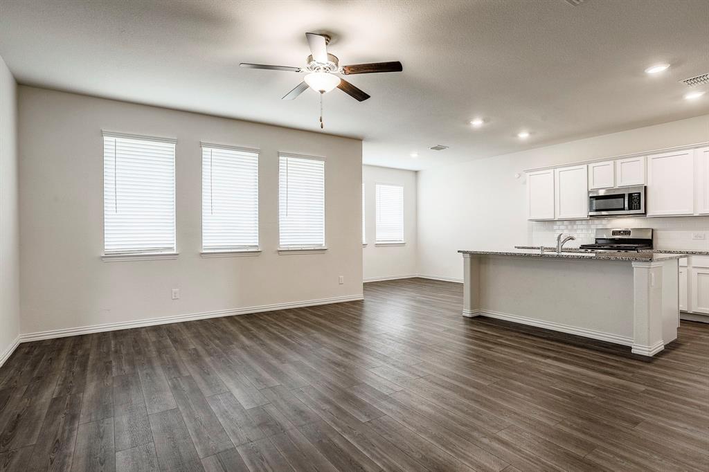 652 Ridgeback Trail Fort Worth, TX 76052 - Photo 9 of 20 Kitchen featuring dark wood-type flooring, a center island with sink, appliances with stainless steel finishes, stone counters, and white cabinets