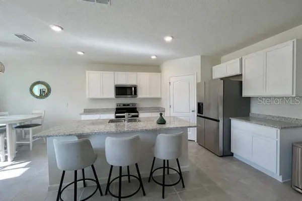 a kitchen with stainless steel appliances granite countertop a dining table chairs refrigerator and microwave