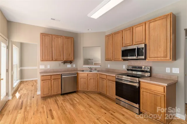 a kitchen with stainless steel appliances granite countertop a stove top oven a sink dishwasher and white cabinets with wooden floor