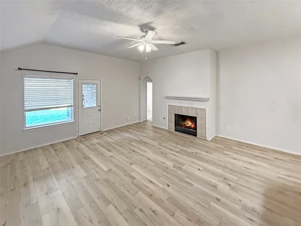 a view of an empty room with wooden floor fireplace and a window