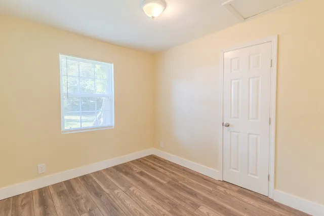 a view of an empty room with wooden floor and a window