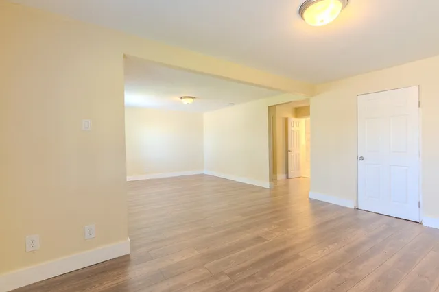 a view of an empty room with wooden floor and window