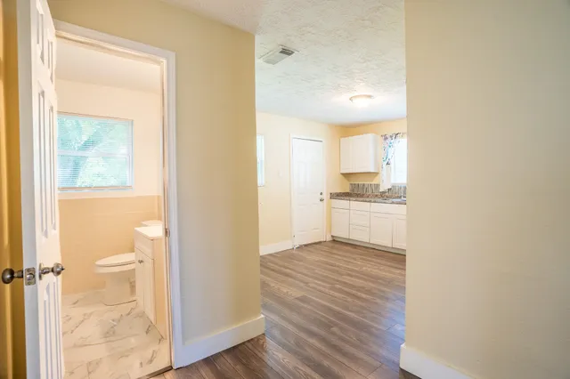 a view of a kitchen from a hallway with wooden floor and a bathroom