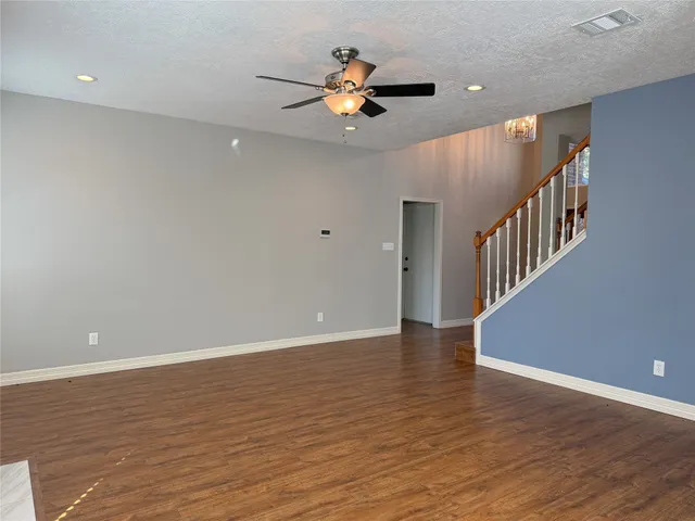 a view of an empty room with wooden floor and a ceiling fan