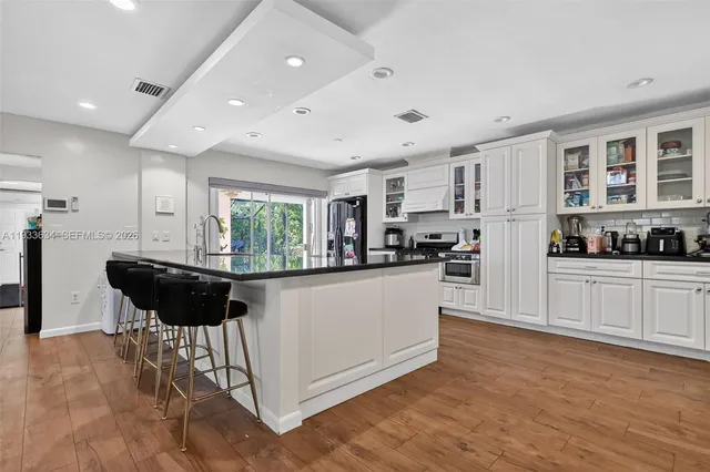 a kitchen with stainless steel appliances kitchen island granite countertop a refrigerator a stove a sink and white cabinets with wooden floor