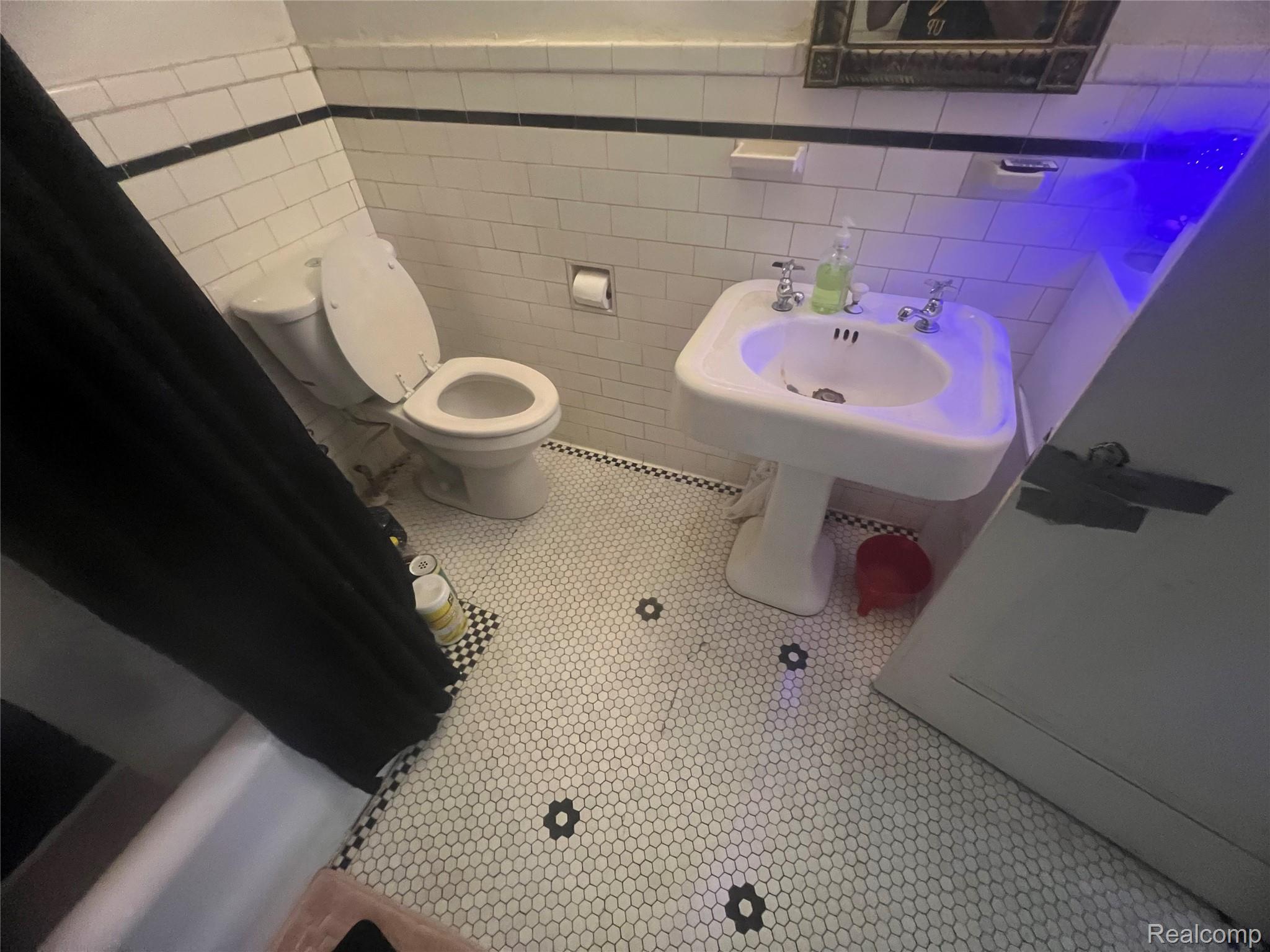 17311 Santa Rosa Drive Detroit, MI 48221 - Photo 84 of 89 Bathroom featuring white subway tile walls with black accent banding, a pedestal sink, and a commode