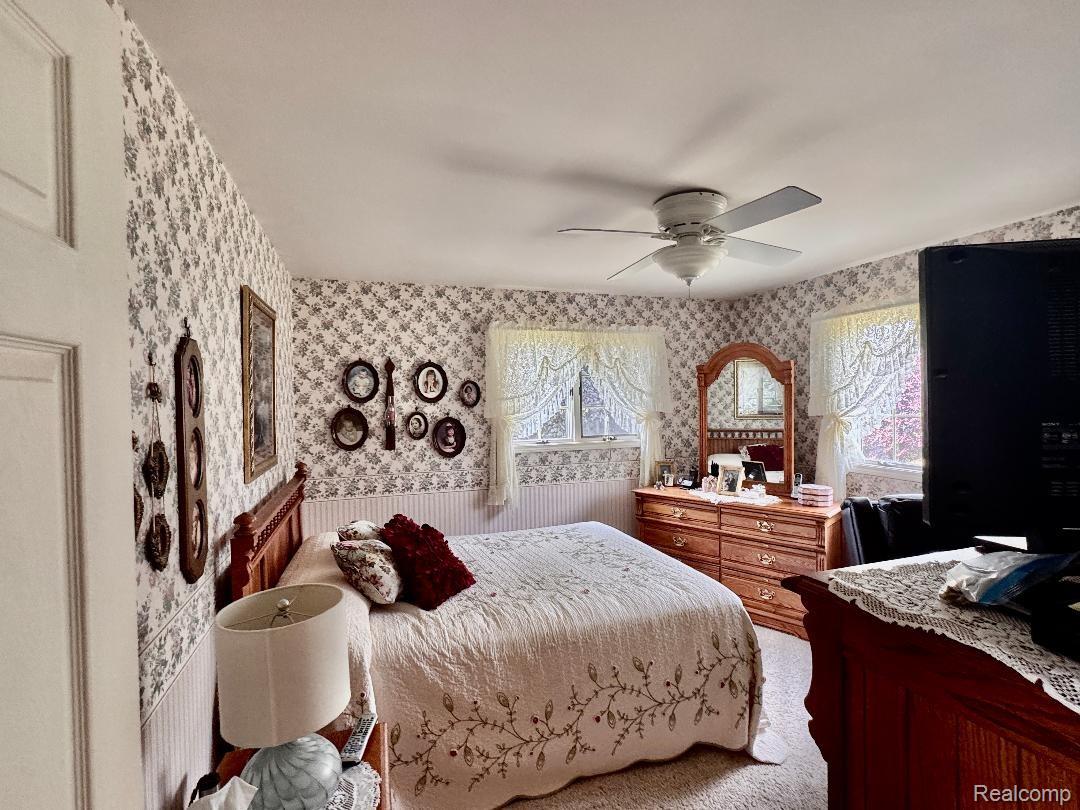 6686 South Schott Road Mayville, MI 48744 - Photo 12 of 25 Bedroom featuring patterned wallpaper, white ceiling fan, two windows with lace curtains, and light-colored carpet flooring
