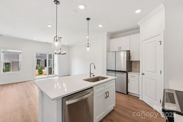 a kitchen with stainless steel appliances granite countertop a sink a refrigerator a stove a kitchen island with wooden floor and cabinets