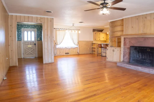 an empty room with wooden floor chandelier fan and windows