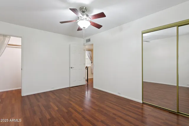 an empty room with wooden floor fan and windows