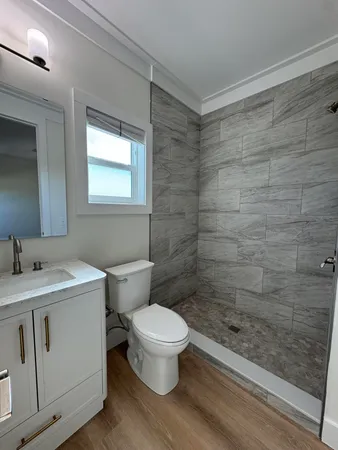 a bathroom with a granite countertop toilet a sink a mirror and a shower