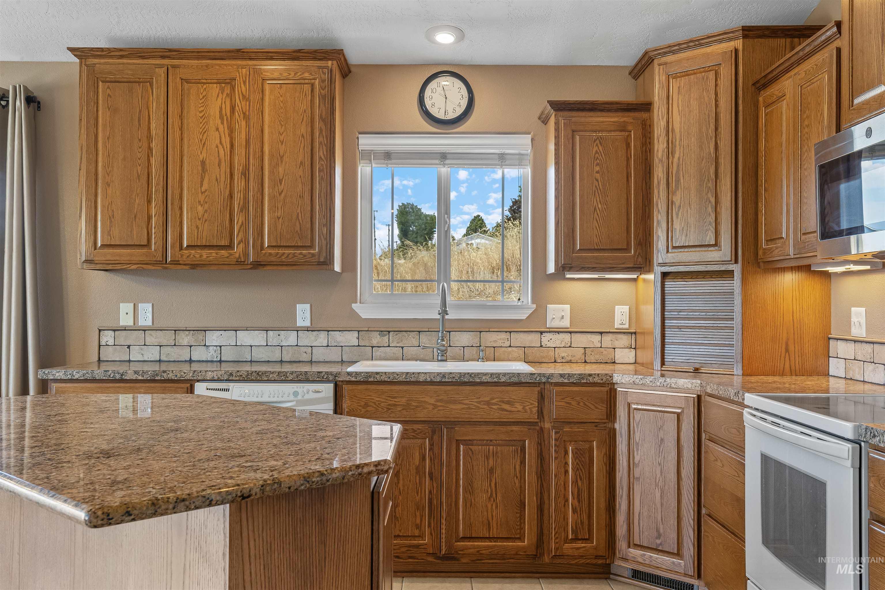 935 Grelle Avenue Lewiston, ID 83501 - Photo 18 of 33 Kitchen featuring white appliances, brown cabinetry, light stone counters, a center island, and recessed lighting