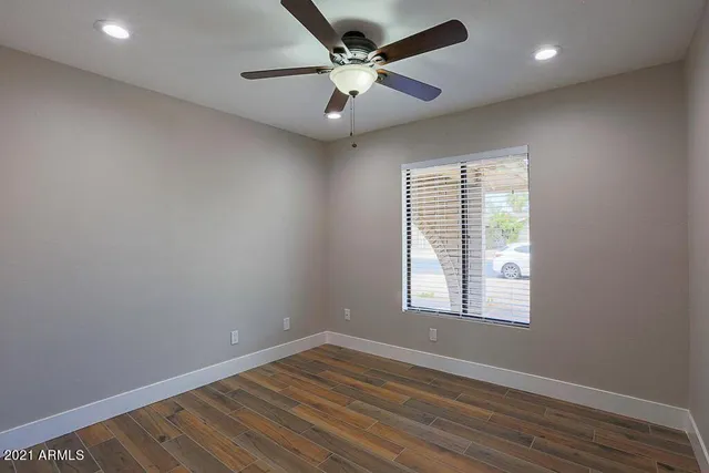 an empty room with wooden floor ceiling fan and windows