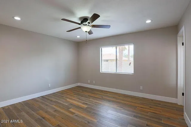 an empty room with wooden floor fan and windows