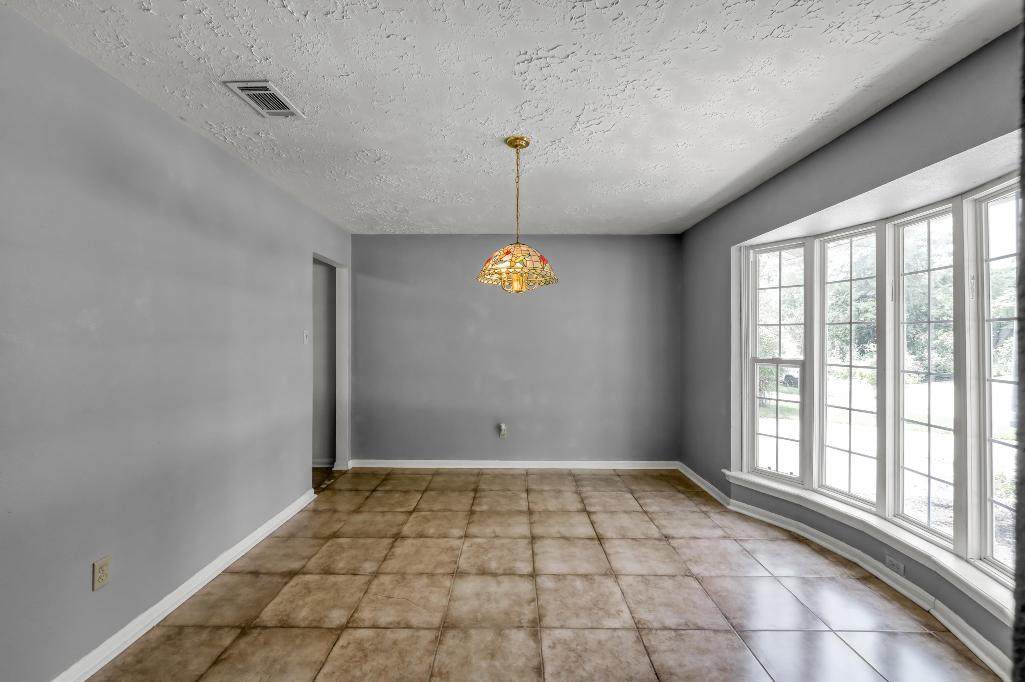 4314 Enchantedgate Drive Spring, TX 77373 - Photo 7 of 47 This room features a spacious area with light gray walls and tiled flooring, illuminated by a decorative hanging light. A large bay window offers abundant natural light and a pleasant view of the outdoors.