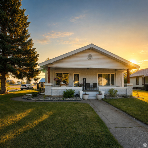 303 North Main Street Grace, ID 83241 - Photo 1 of 22 Single-story residence featuring a covered front porch with brick pillars and siding, a concrete pathway, a manicured lawn, and mature landscaping