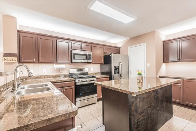 a kitchen with kitchen island granite countertop a stove top oven a sink a counter space and cabinets